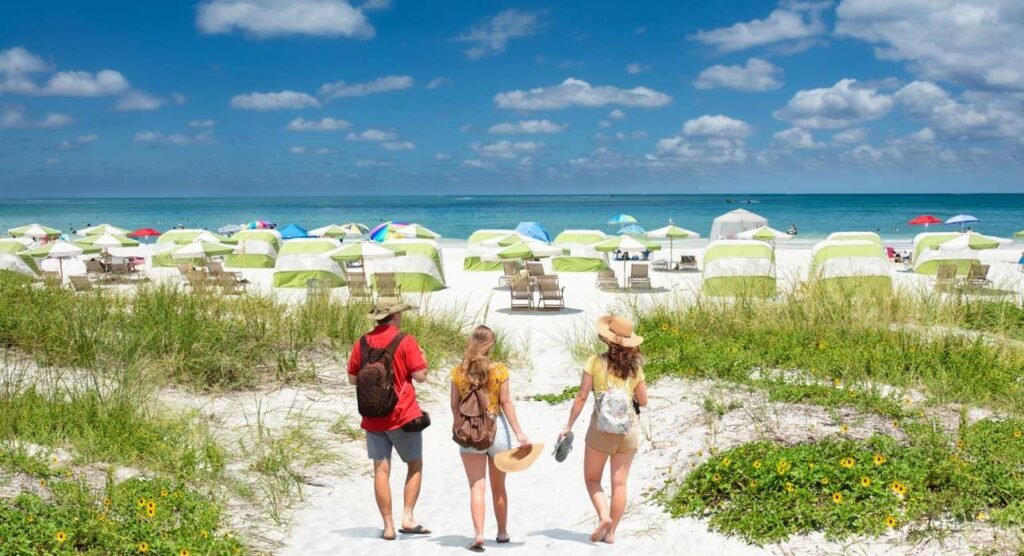 Family walking on beautiful white sand beach on summer vacation in Florida Beach umbrellas and chairs on the beach, green ocean in background. Clearwater Beach, Florida, USA.