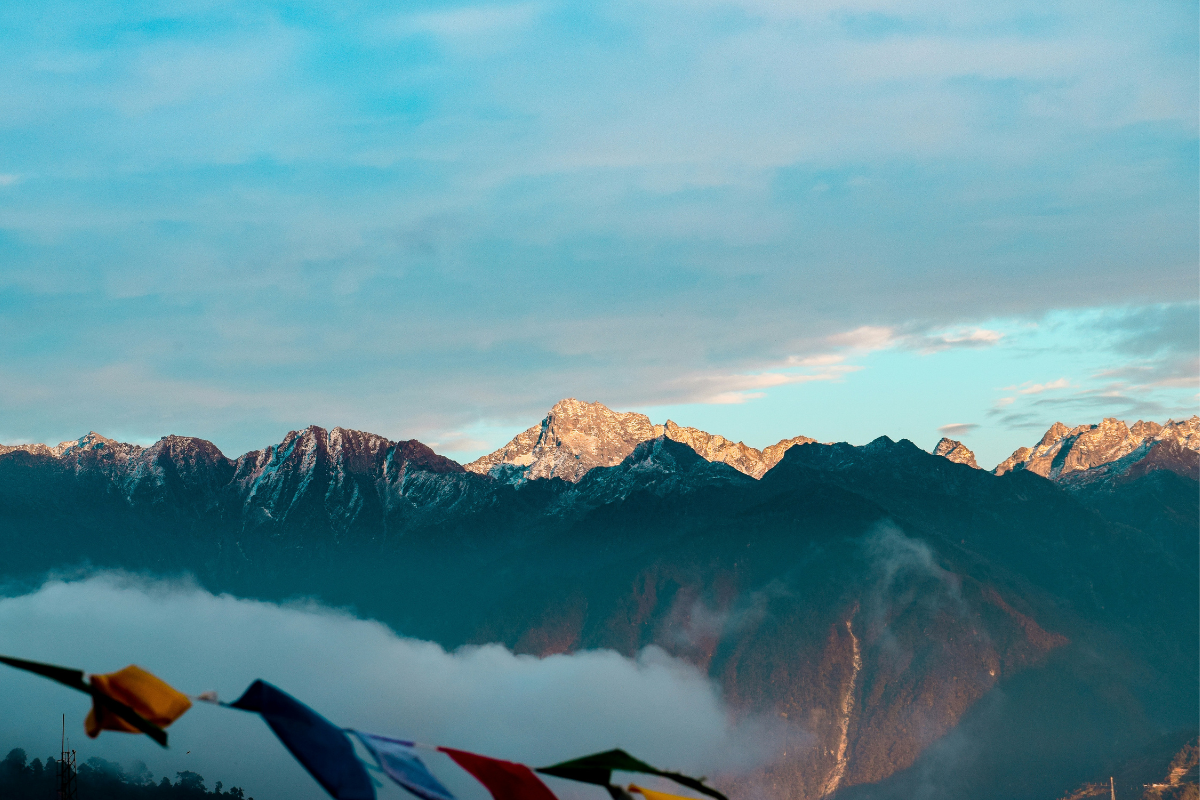 Golden sunrise over Himalayan peaks with clouds and colorful prayer flags in Arunachal Pradesh.