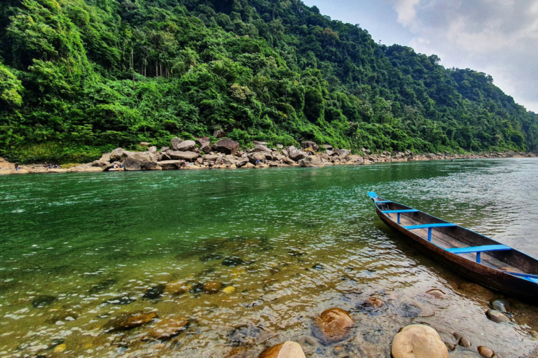 Transparent river water with wooden boat and lush green hills in Dawki Umngot River Meghalaya.