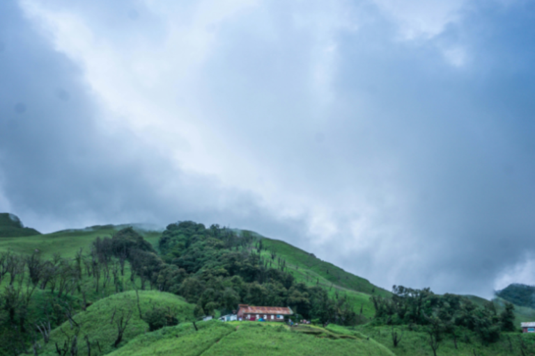 Lush green hills with a small house and misty clouds in North East India landscape.